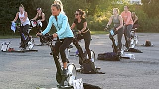 Jackie Brennan, of Merrimac, Mass., front, pedals on a stationary exercise bike with others during a spinning class in a parking lot outside Fuel Training Studio