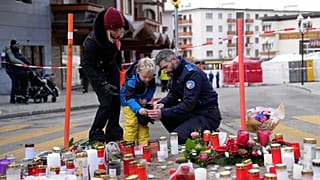 A police officer helps a boy to light a candle near the sealed off Le Constellation bar in Crans-Montana, Swiss Alps, 2 January 2026