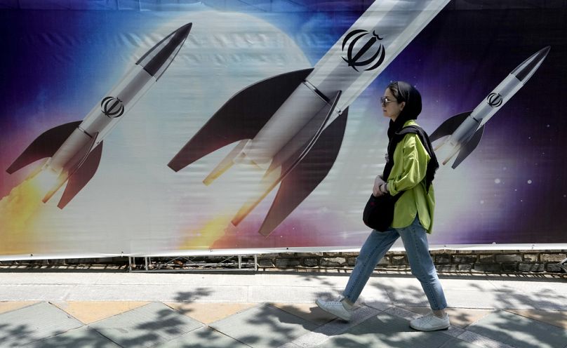 FILE: A woman walks past a banner showing missiles being launched, in northern Tehran, 19 April 2024
