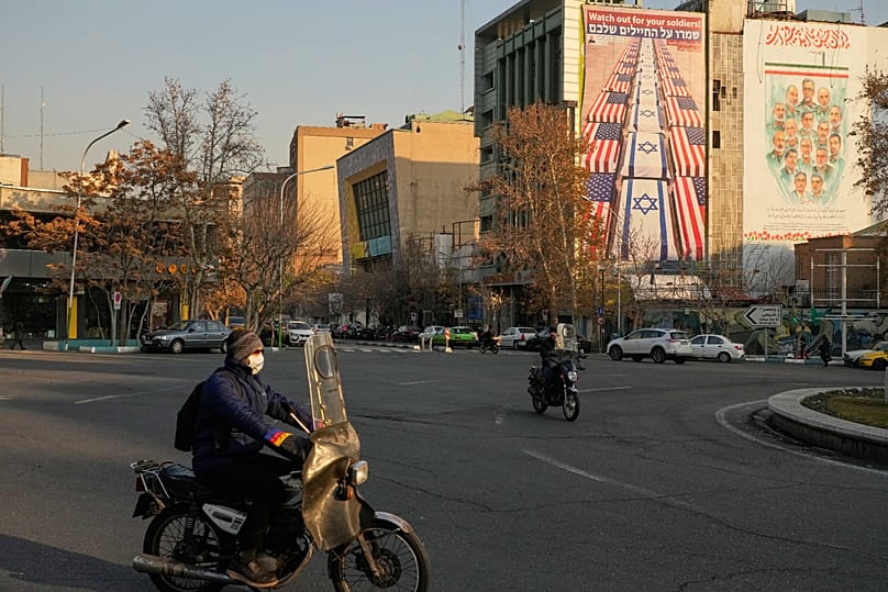 People on motorbikes drive past banners containing an anti-US and anti-Israel image in Tehran, 4 January, 2026