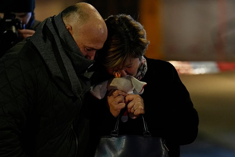 A woman holding a stuffed animal, whose daughter is missing, stands near the sealed-off Le Constellation bar in Crans-Montana, Switzerland, Friday, Jan. 2, 2026.