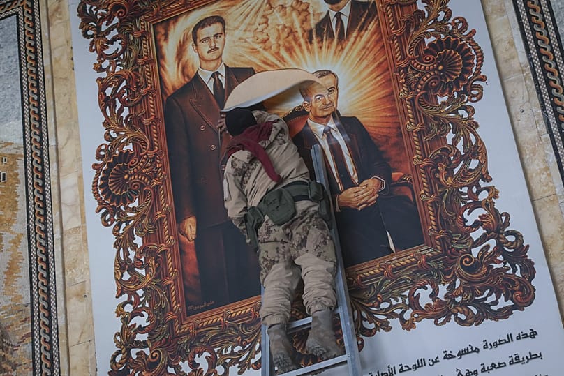 A Syrian opposition fighter tears a painting depicting Syria’s overthrown President Bashar al-Assad and his late father Hazef at Aleppo International Airport, 2 December, 2024